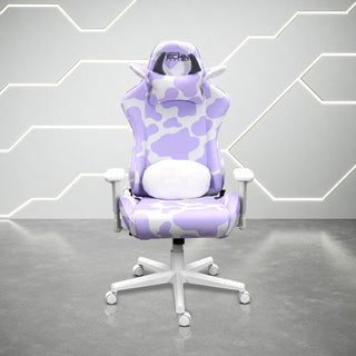 Front view of the techni sport cow gaming chair in lavender in a white room with grey floor. This cute gaming chair features a white base, with white and lavender cow print. The cow chair headrest pillow has grey horns and ears lined with fluffy white material and the lumbar pillow has matching fluffy white to compliment the design. The purple gaming chair of your dreams, perfect for a cute gaming setup.